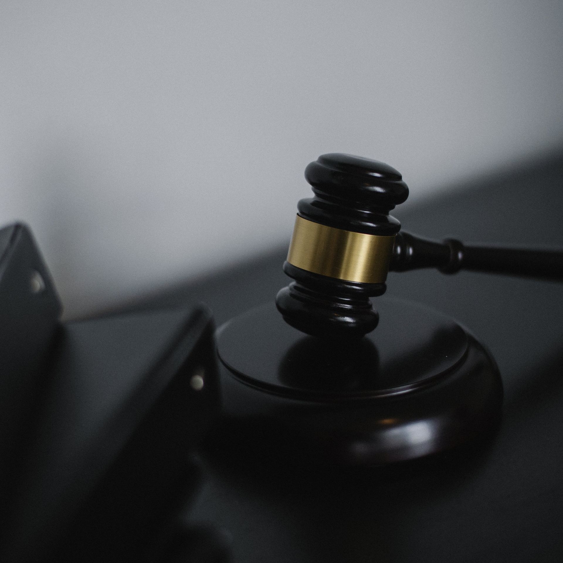 Judge’s gavel on a round base beside a closed black folder in a dim gray setting