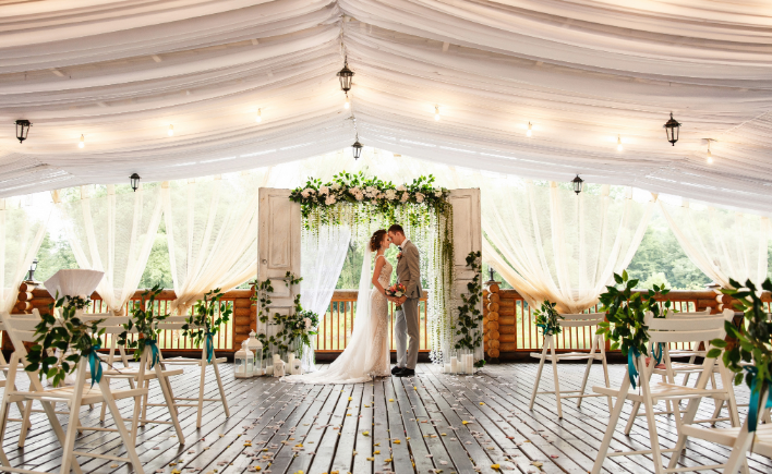 Bride and groom kissing under a draped marquee with fairy lights