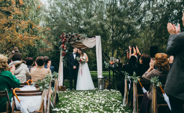 Guests watching a couple marry under a white arch in a garden