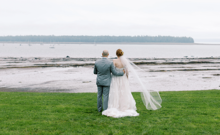 Bride and groom standing on a lawn overlooking the water