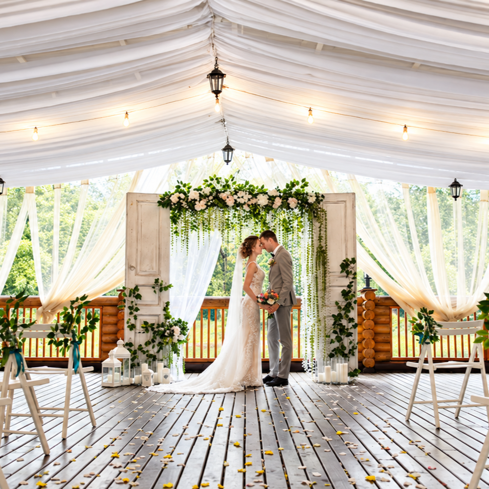 Bride and groom kissing under a draped marquee with fairy lights