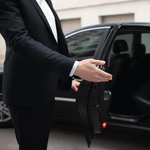 Man in suit opening a car door, offering assistance.