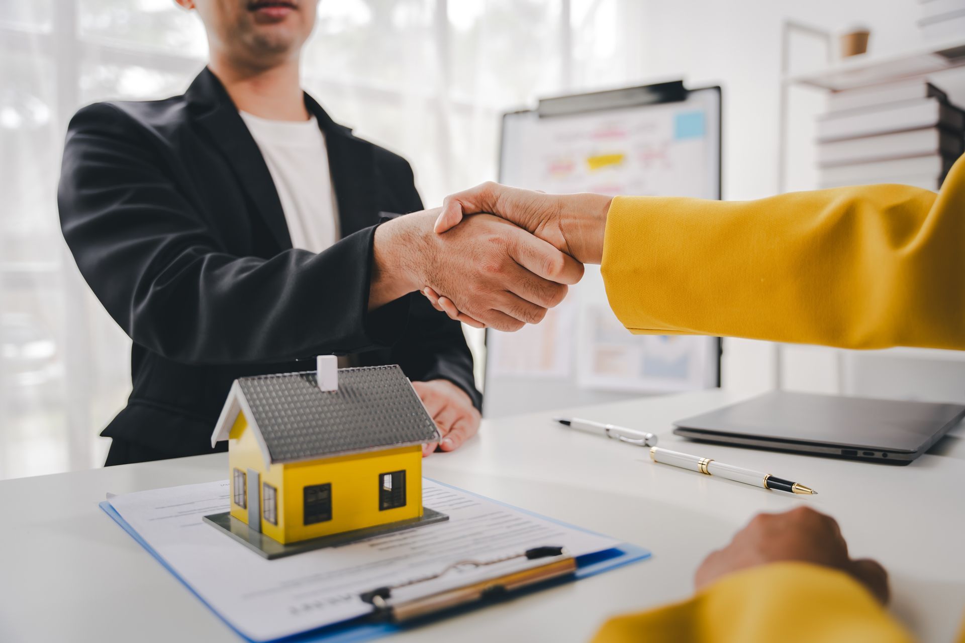 A Man and a Woman Are Shaking Hands Over a Model House