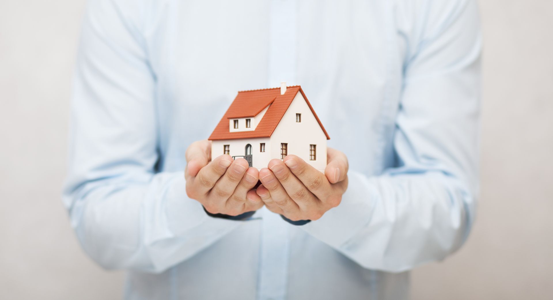 A Man is Holding a Small Model House in His Hands