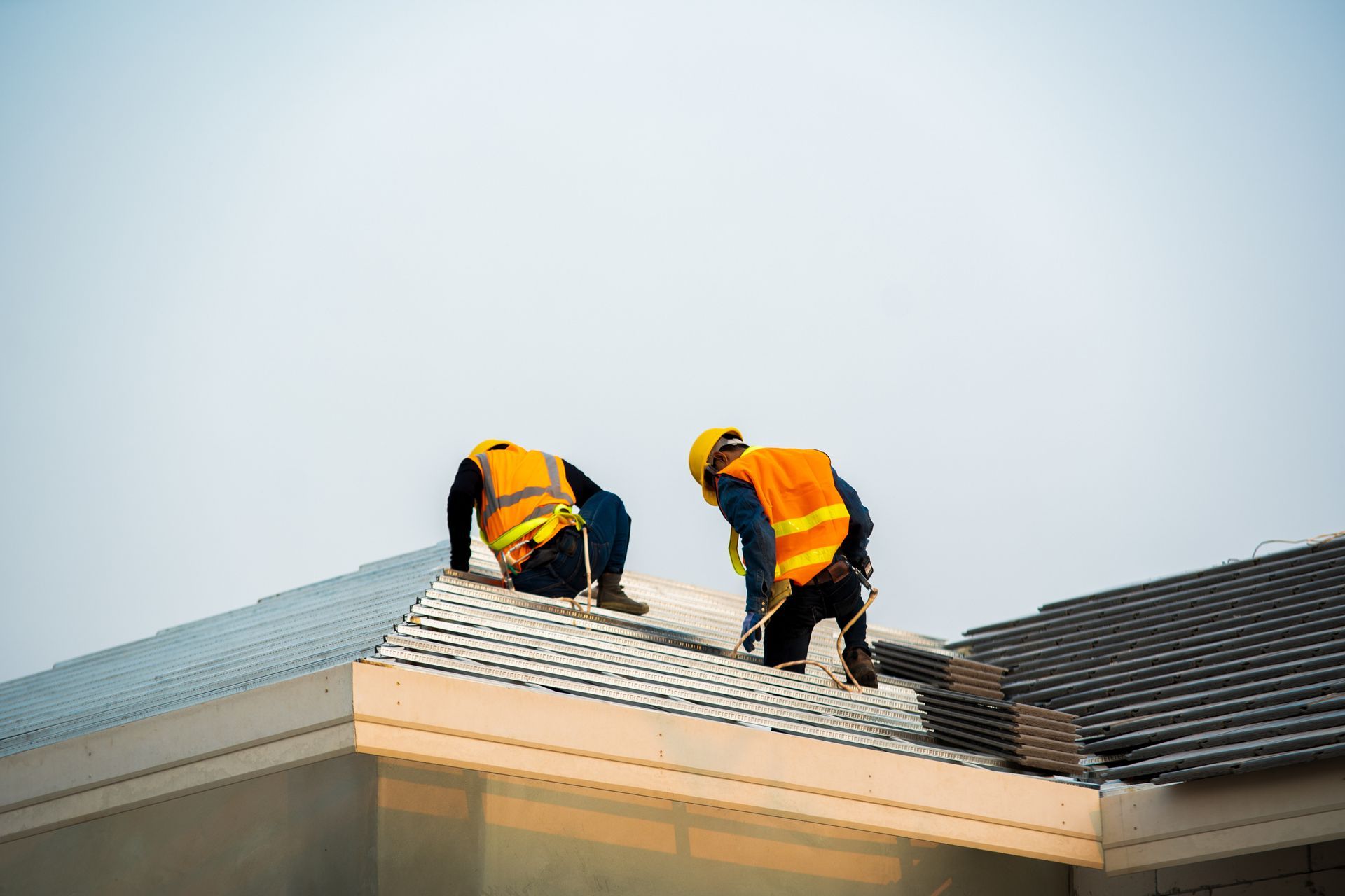 Two construction workers installing metal roofing panels on a building roof. Two construction workers installing metal roofing panels on a building roof.