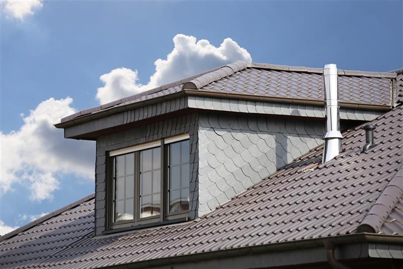 Gray roof with dormer window, chimney, and blue sky with clouds.