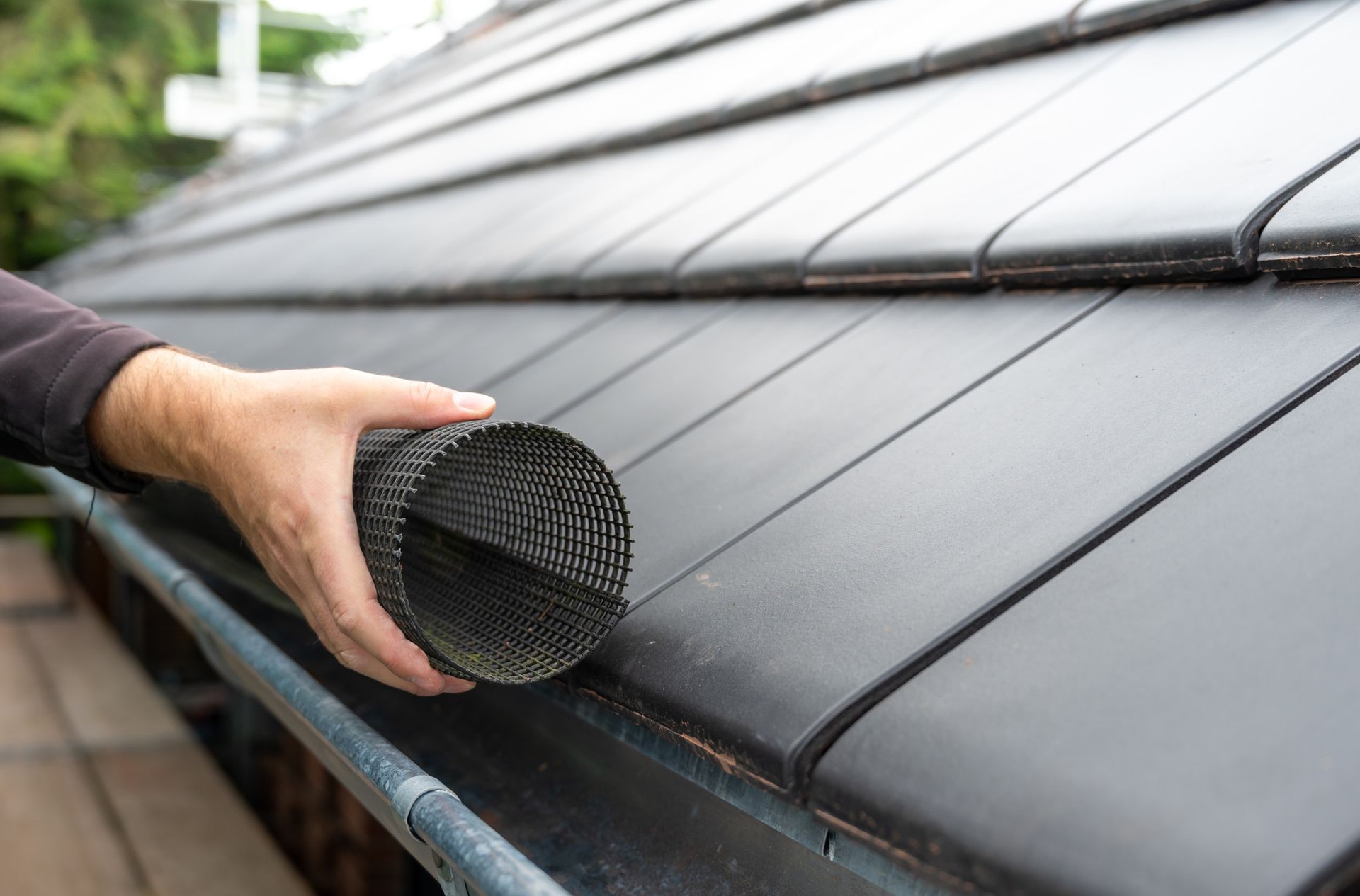 Person installing black mesh gutter guard on a roof.