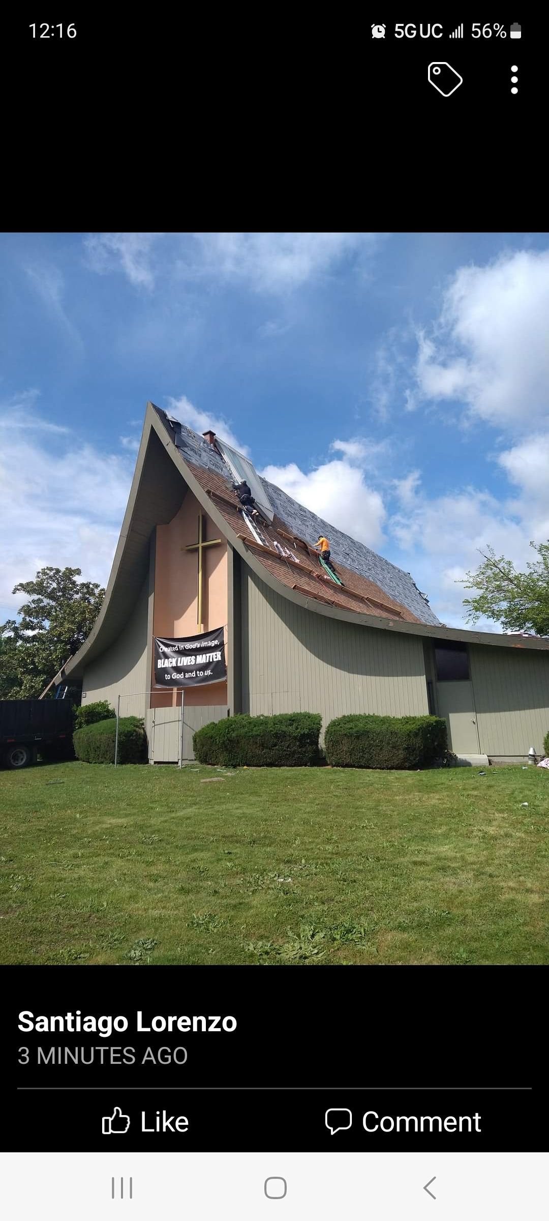 A church building with roof damage, under a blue sky, surrounded by green grass.