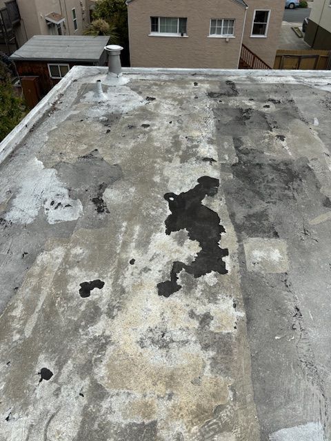 Overhead view of a flat roof with weathered, gray and black spots, and a metal vent.