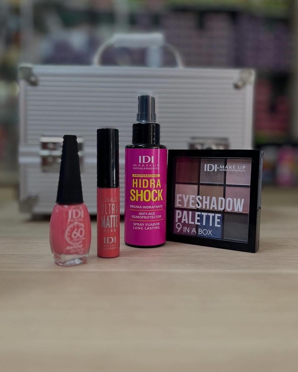 Sobre una mesa hay productos cosméticos, entre ellos pintalabios, brillo de labios, spray y una paleta de sombras de ojos.