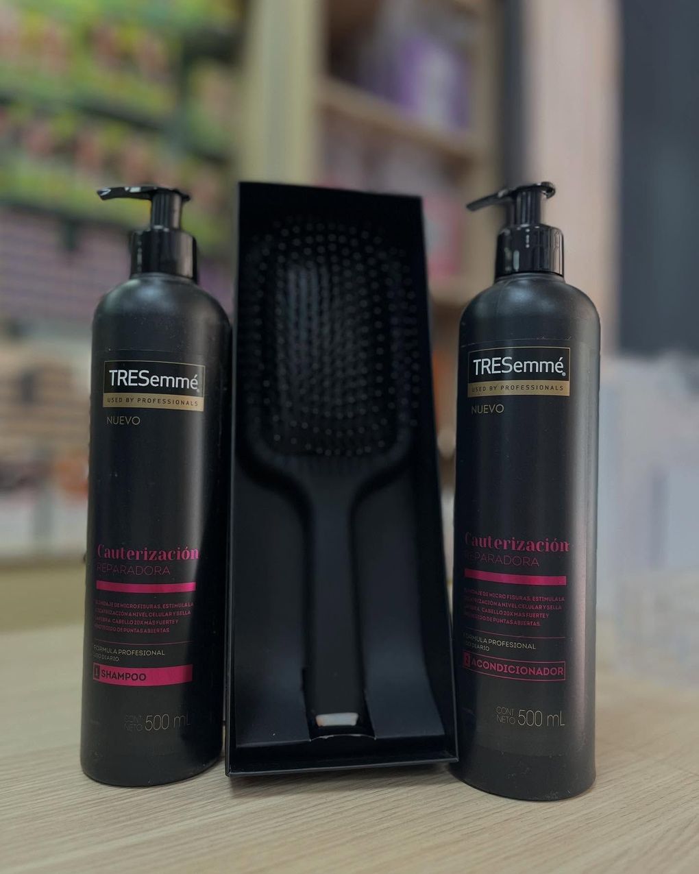 Dos botellas negras con dosificador flanquean un cepillo de pelo negro sobre una mesa.