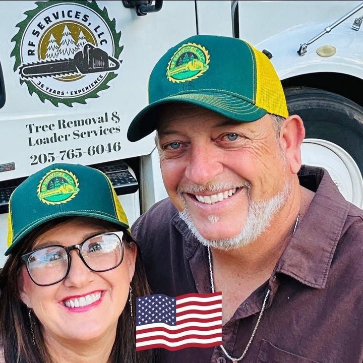Smiling person in a yellow shirt and green cap standing outdoors by a tree.