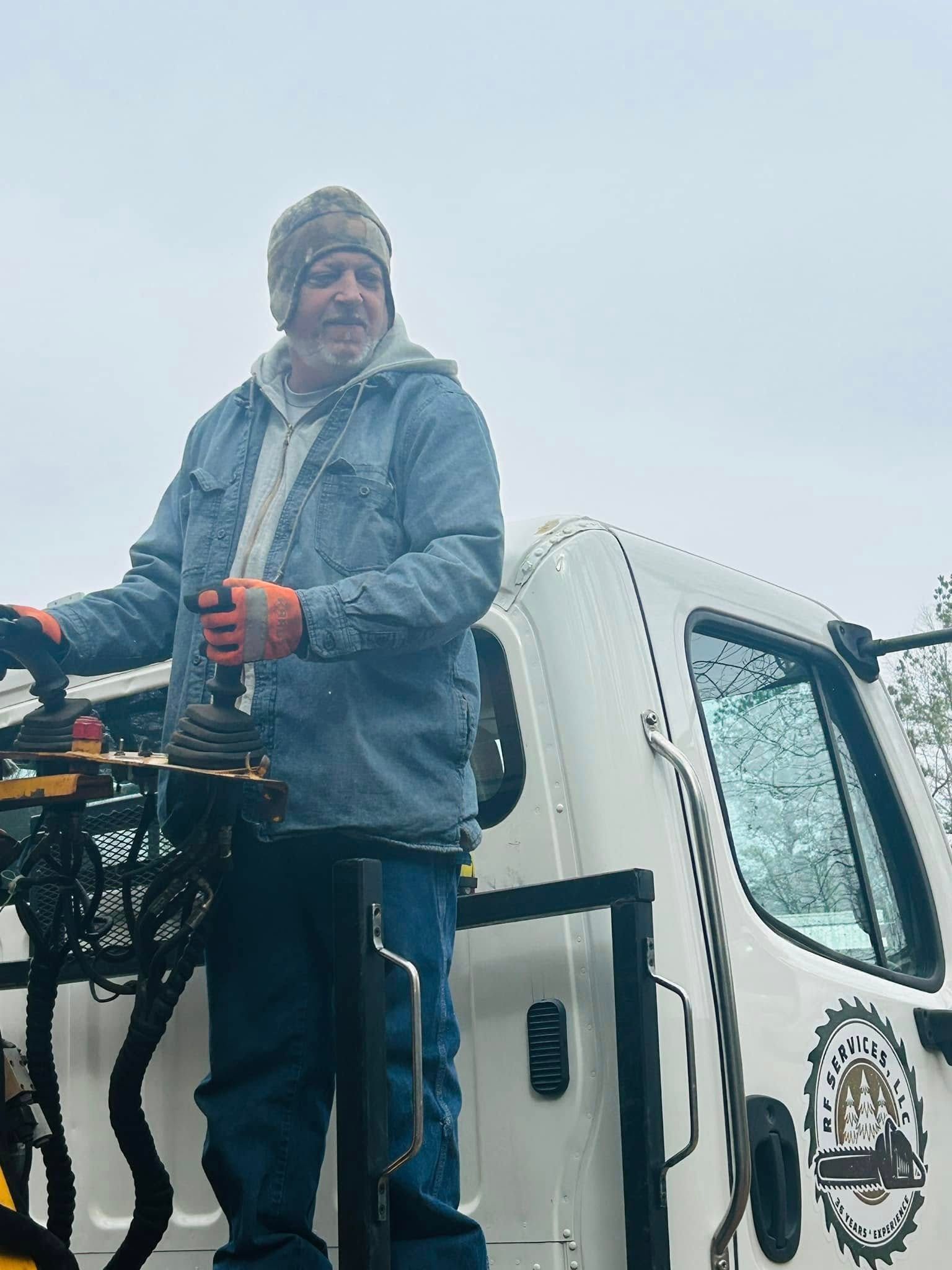 Person in winter gear standing on a truck lift, holding controls in snowy weather.