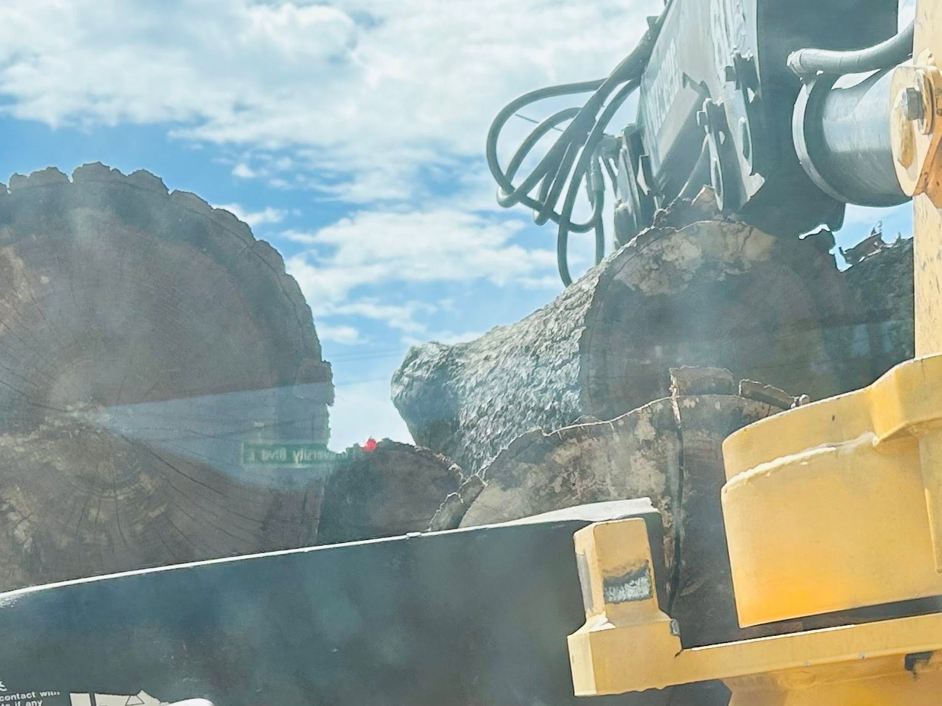 Construction machinery beside large rocks and yellow containers under a blue sky