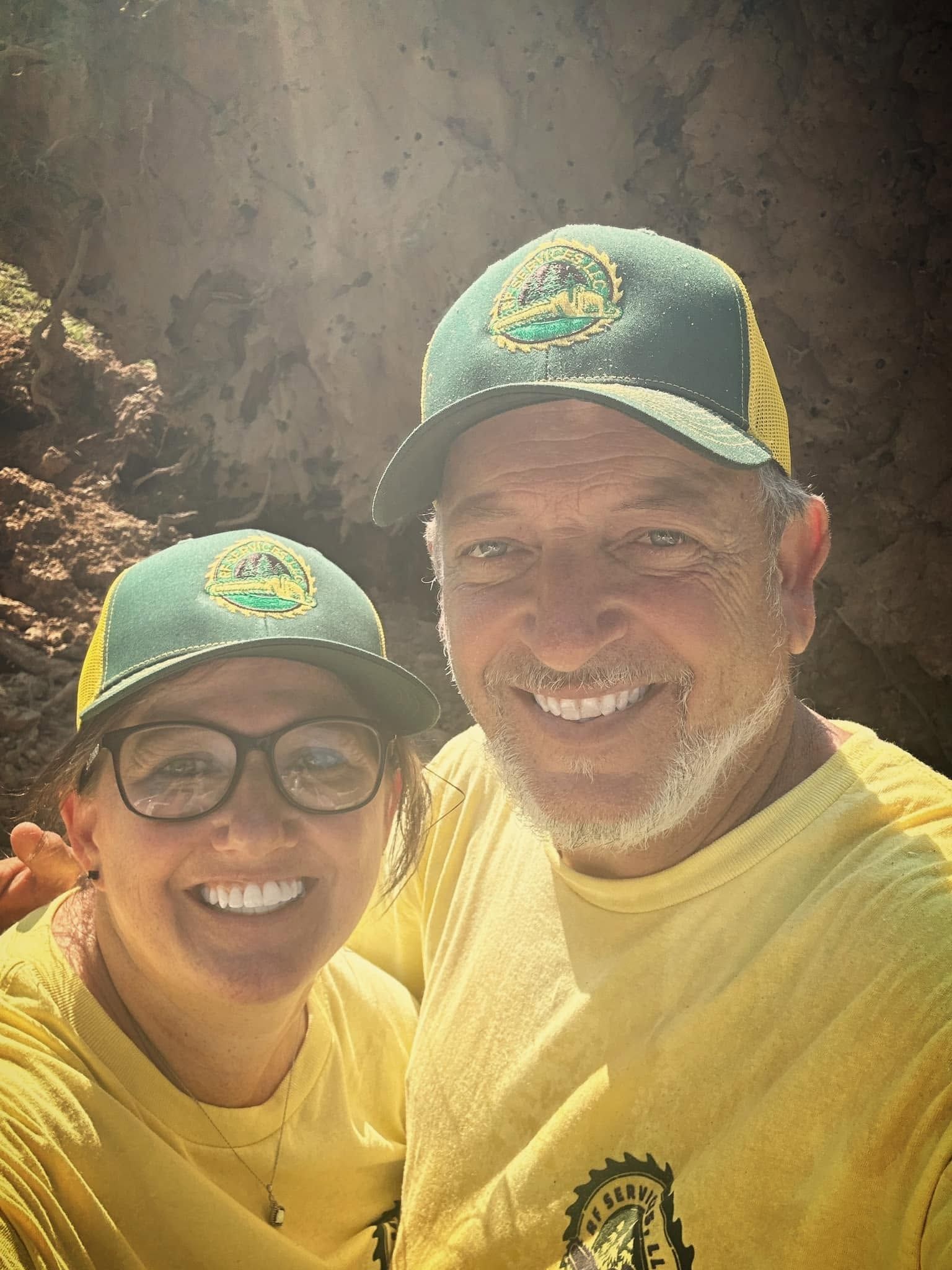 Two smiling people in yellow shirts and caps posing outdoors in bright sunlight