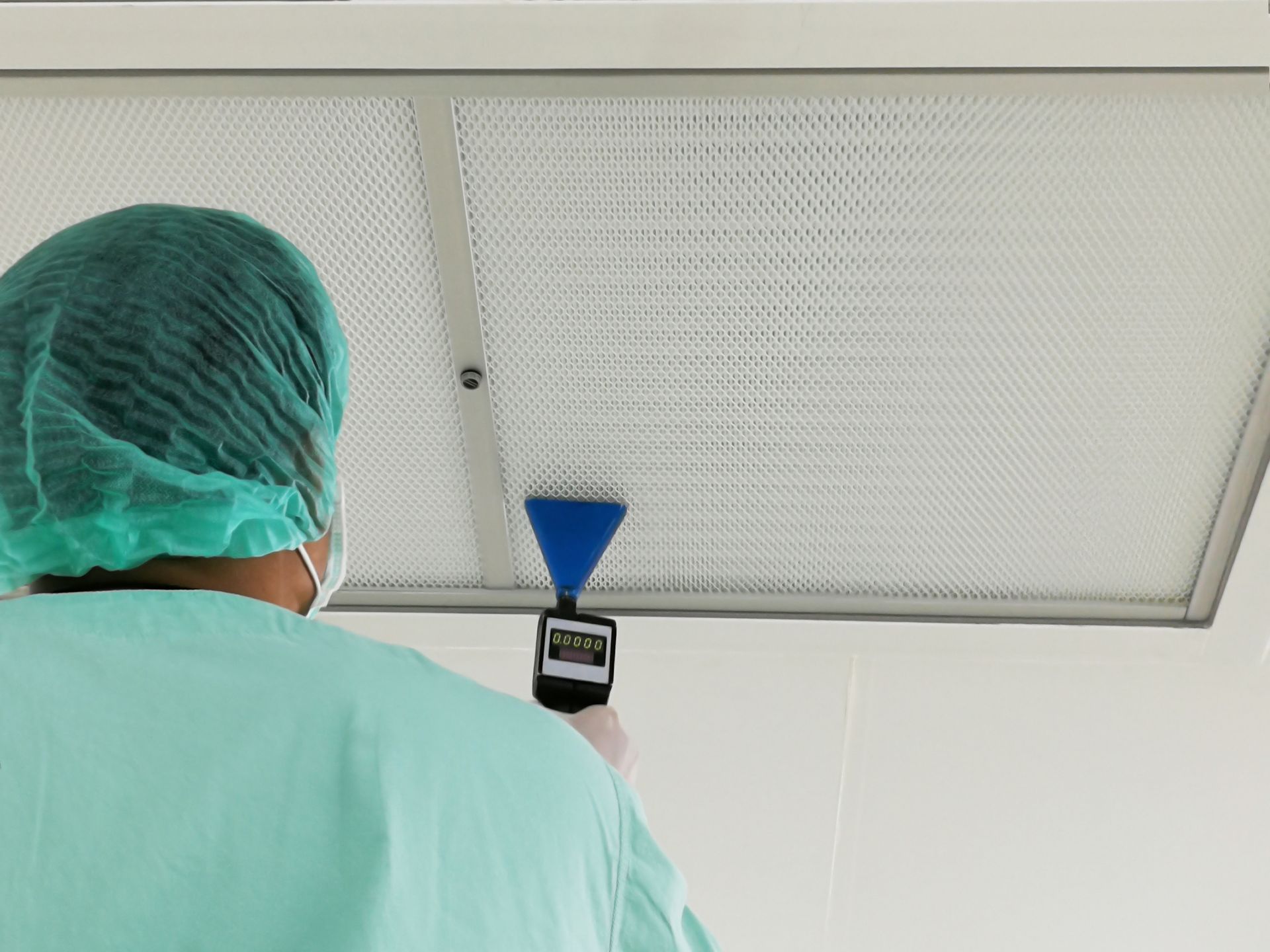 Technician in protective clothing testing a ceiling air filter with an inspection device.