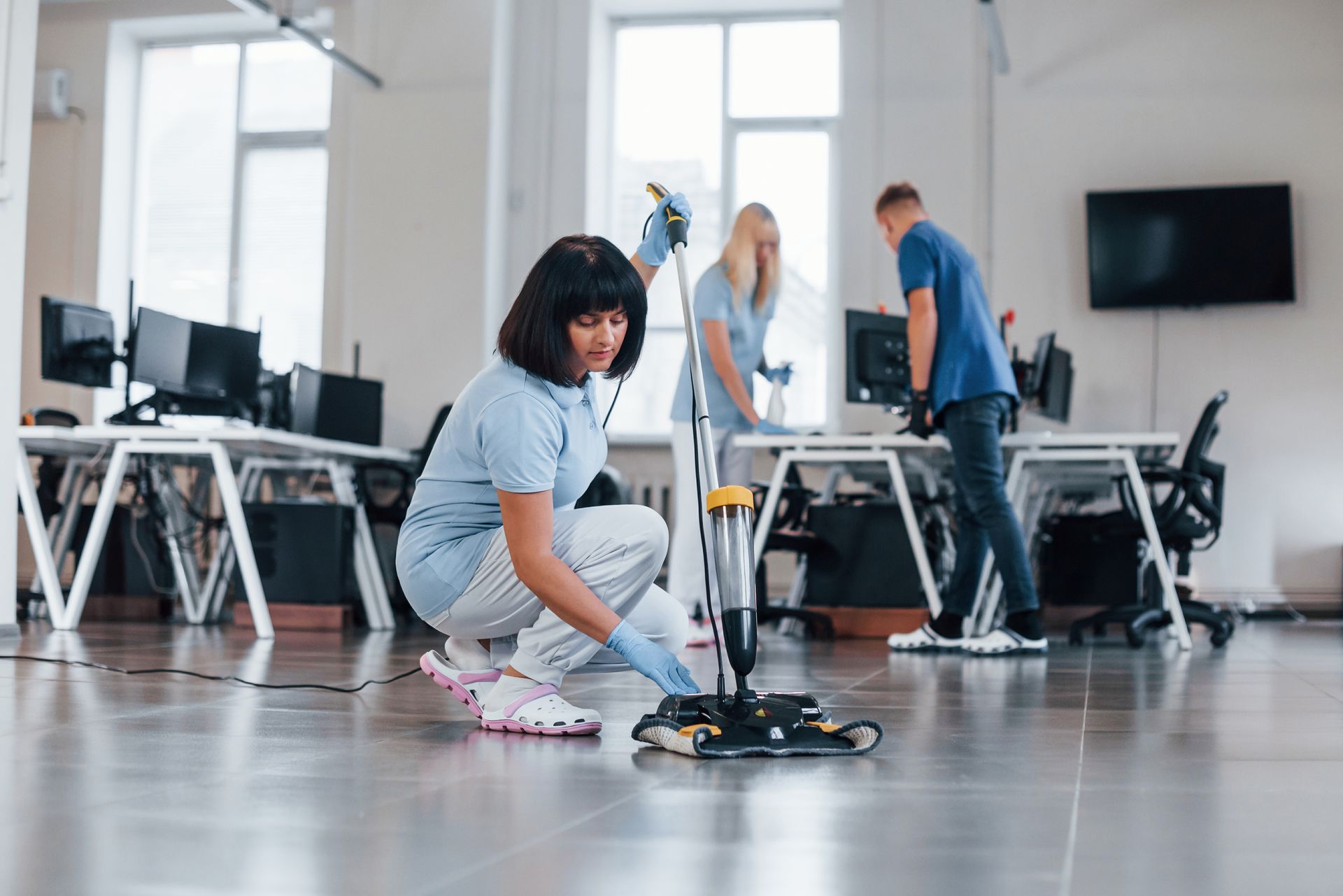 A woman is cleaning the floor of an office with a mop.