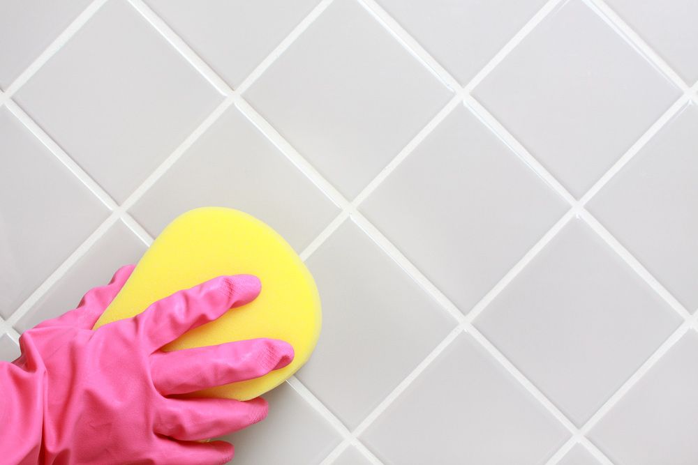 A Person Wearing Pink Gloves Is Cleaning A Tile Wall With A Yellow Sponge — Big Red Carpet & Property Maintenance In Bowen, QLD