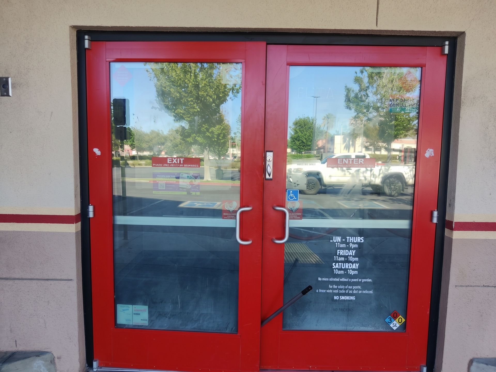 Red double glass doors with silver handles in a beige building facade.