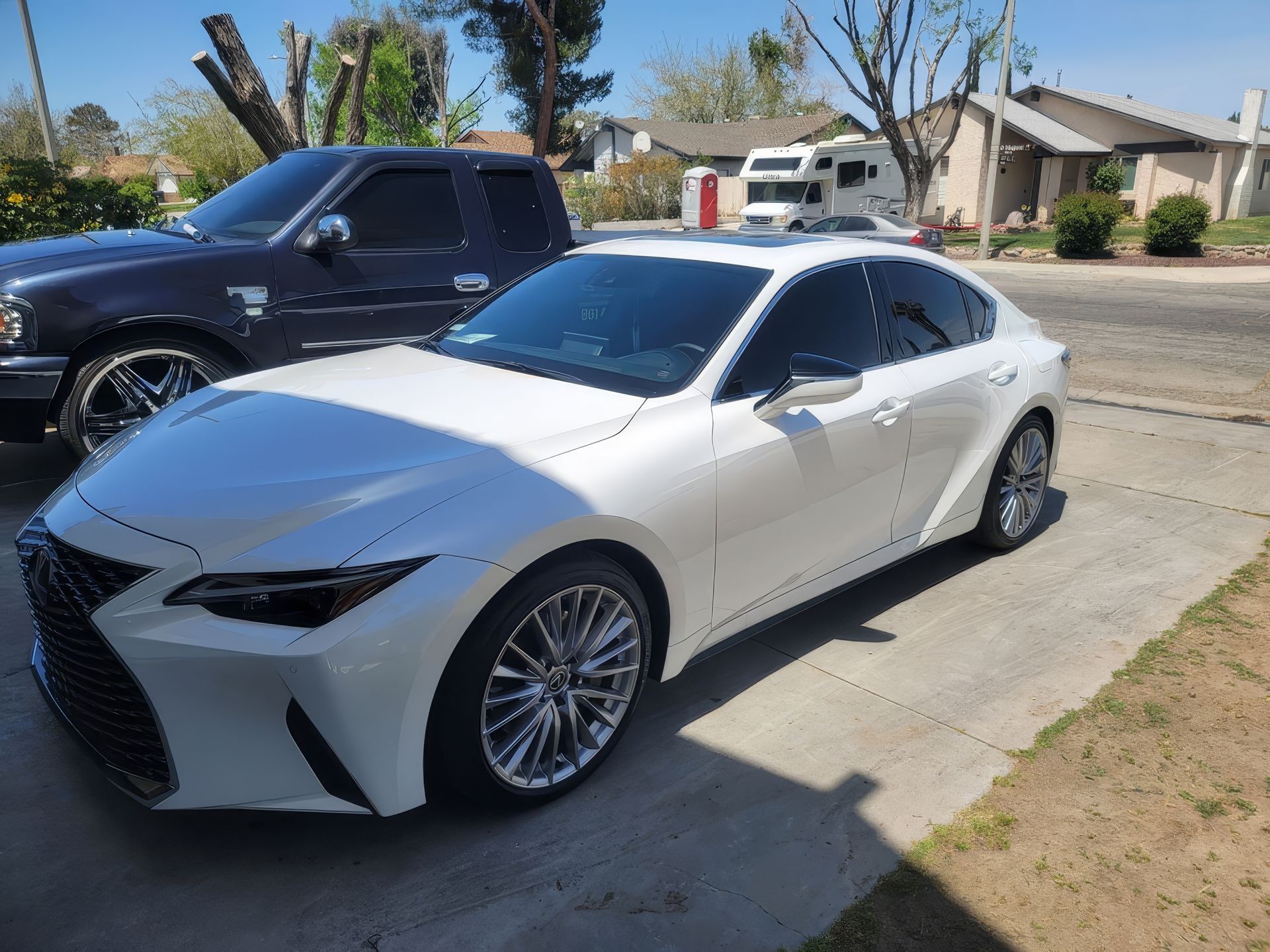 White sedan parked in a sunny driveway beside a black truck in a suburban neighborhood
