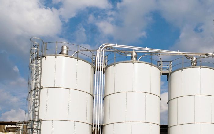 A row of white silos against a blue sky with clouds.
