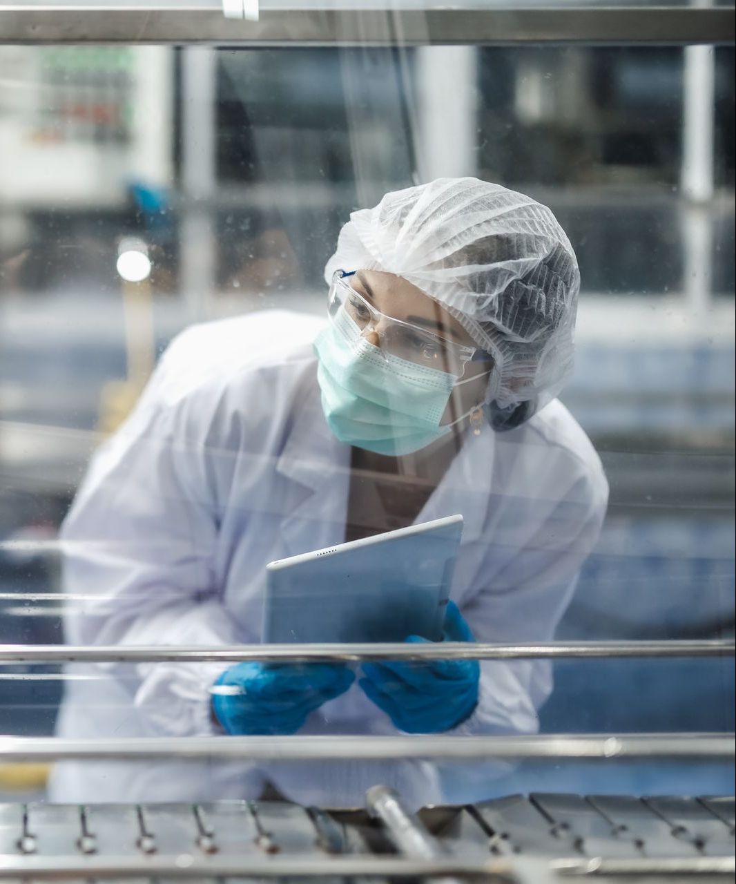 A woman in a lab coat and mask is looking at a tablet.