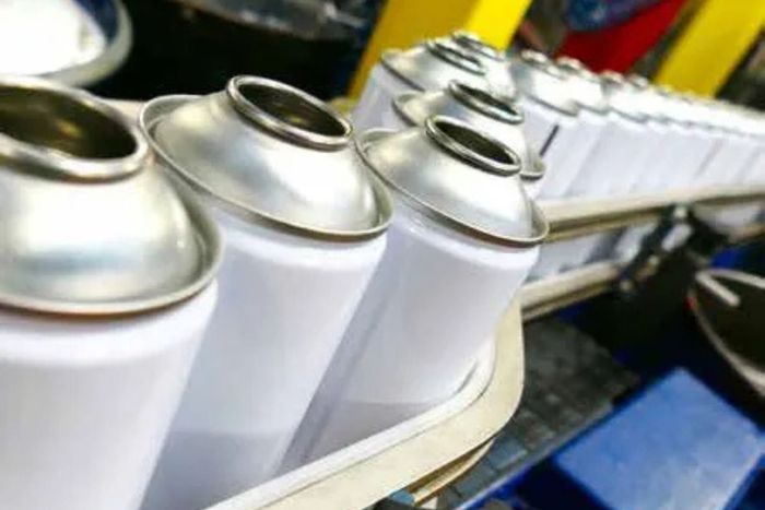 A bunch of spray cans are lined up on a conveyor belt.