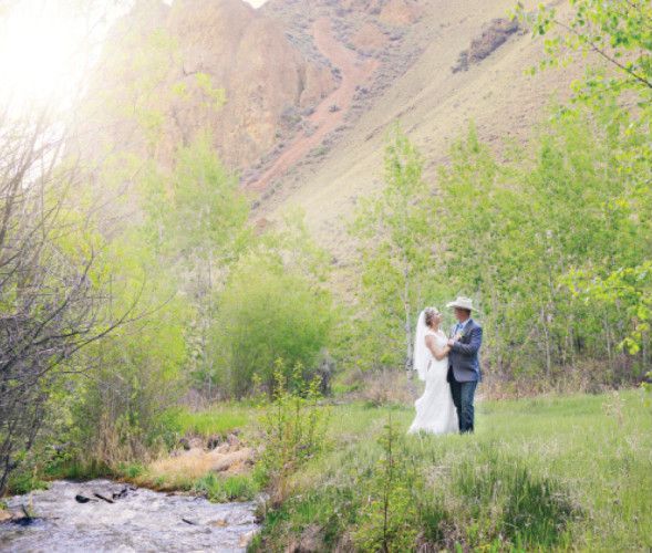 A bride and groom are standing next to a river in a field.
