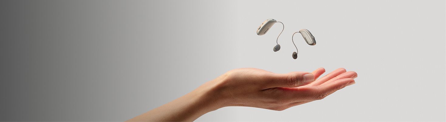 ReSound Sensia hearing aid and charging accessory resting above an open palm