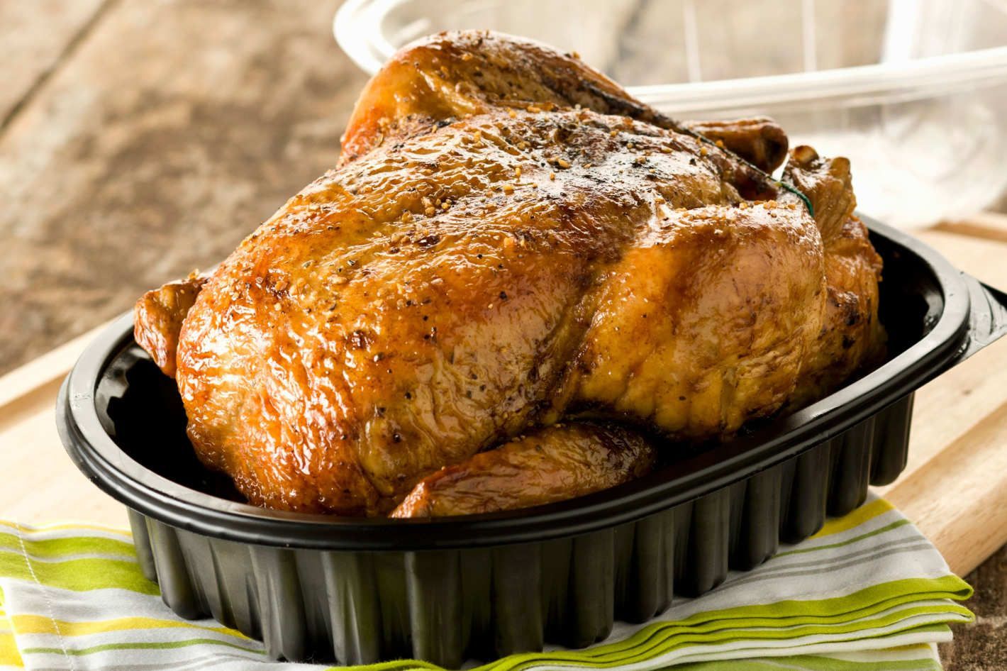 Roasted chicken in a black baking dish on a striped cloth, with a golden-brown crispy skin