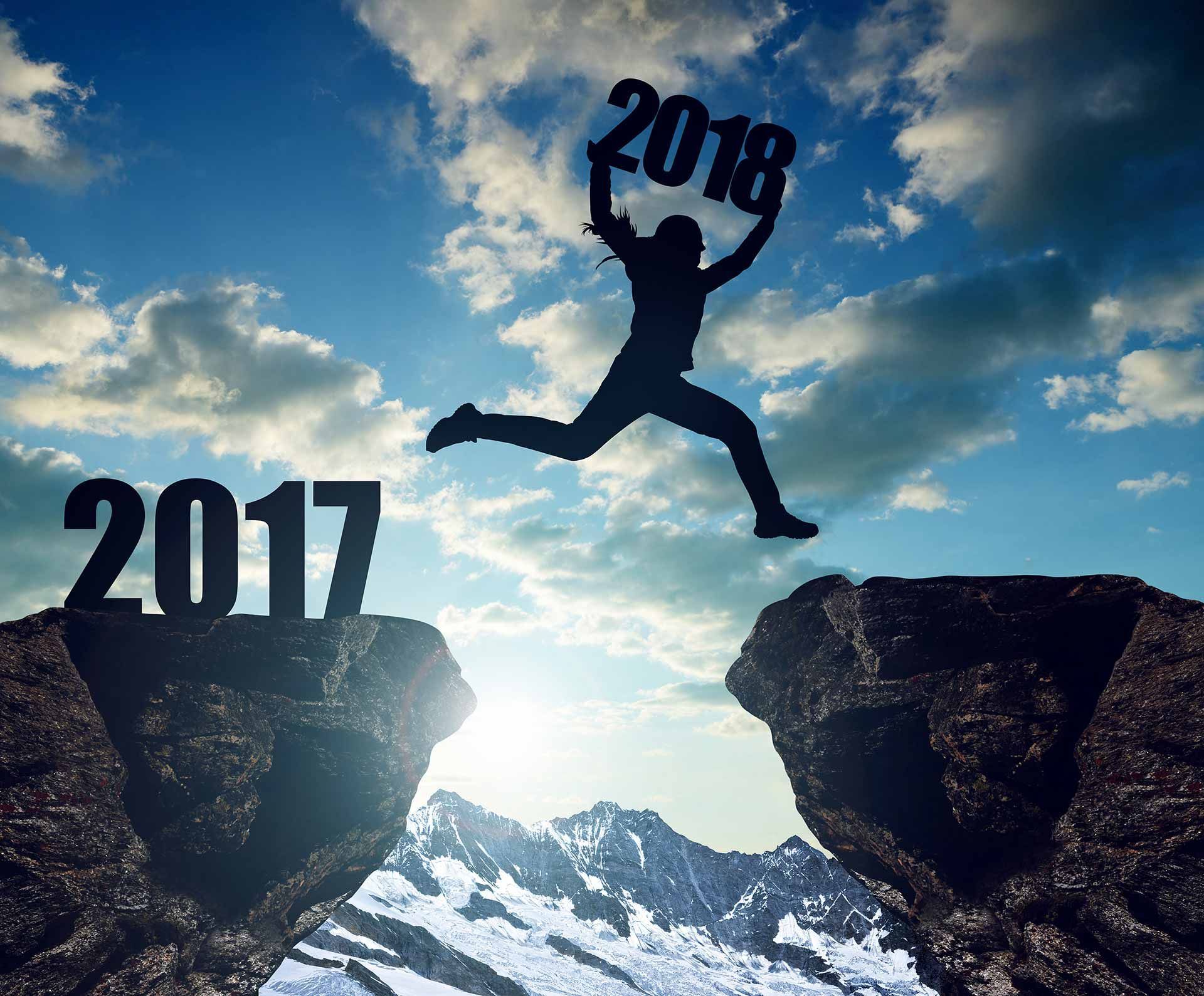 Silhouette of a person leaping from 2017 to 2018 across a mountain gap at sunrise