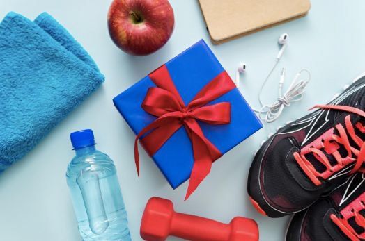 Fitness gear and gifts on a blue surface, including sneakers, dumbbell, water bottle, apple, and red gift box