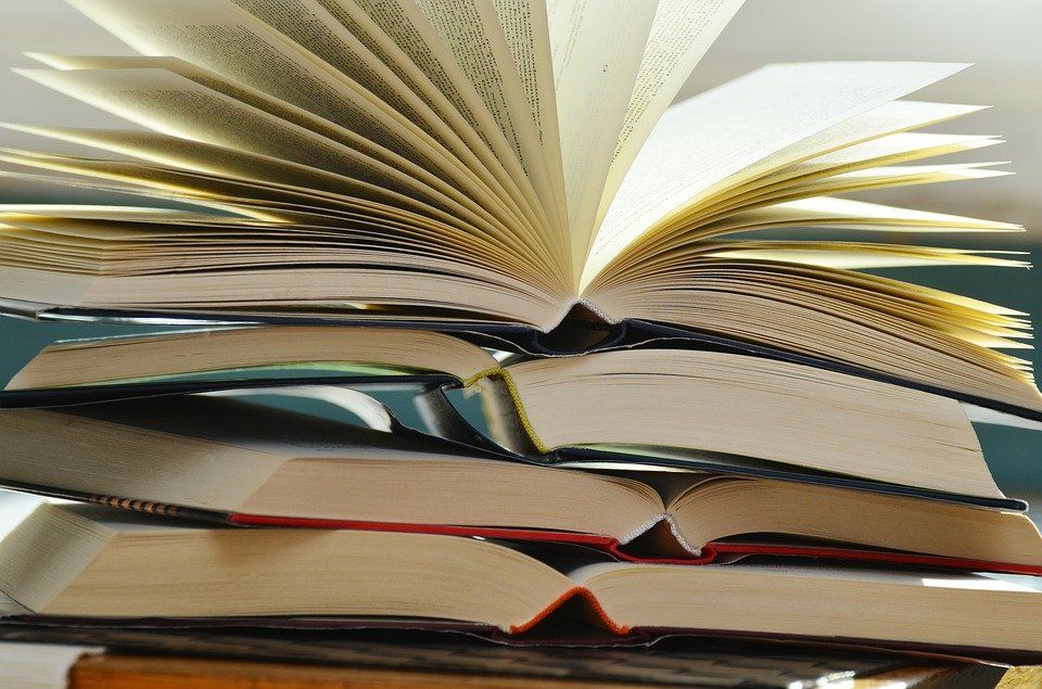 Stack of books with an open book fanned out on top, pages lit warmly