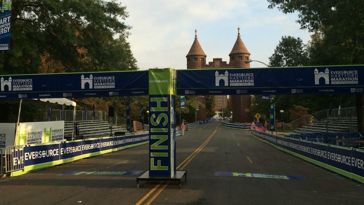 Road race finish line banner on an empty street, with a cathedral in the distance at dusk.