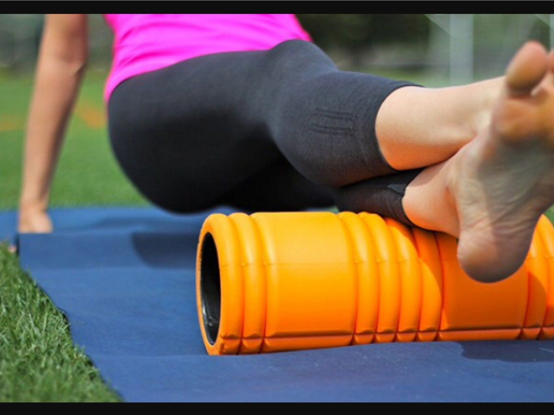 Person using an orange foam roller on a blue mat during an outdoor workout