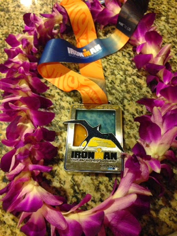 Purple orchid lei with an Ironman medal ribbon on a speckled stone surface