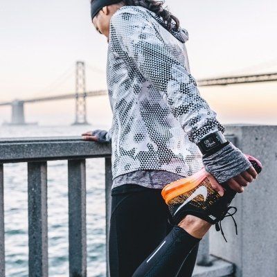 Runner stretching by a waterfront railing at sunset, with a bridge in the background.