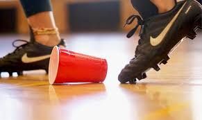 Two soccer players’ cleats near a fallen red plastic cup on an indoor court