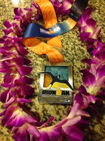 Purple flower lei with a blue-and-orange ribbon and a small Iron Man medal on a stone surface