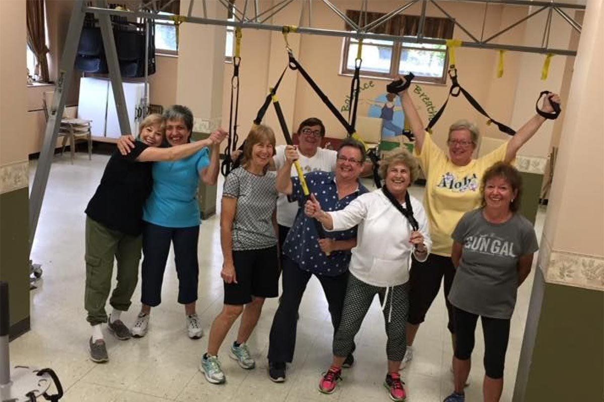 Group exercising in a gym with resistance bands, smiling and posing mid-workout.