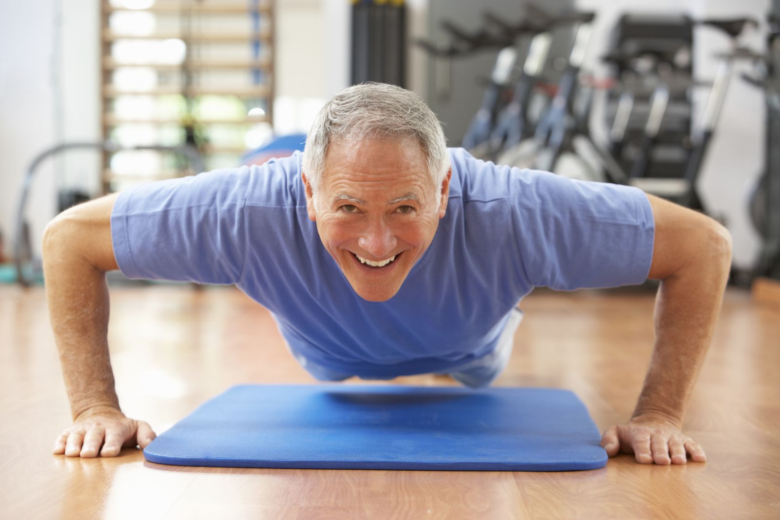 Man smiling while doing a push-up on a blue mat in a gym