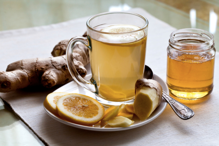 Glass of ginger tea with lemon slices and fresh ginger on a plate, plus a jar of honey on a table
