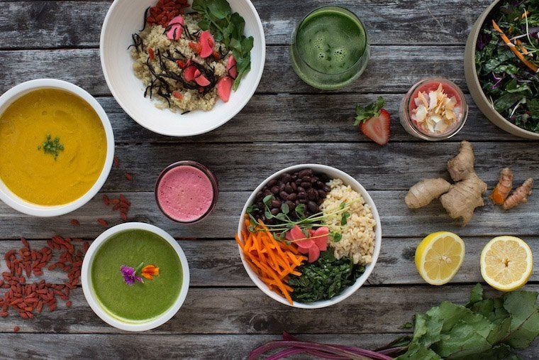 Colorful vegan bowls and drinks arranged on a rustic wooden table with lemons and herbs