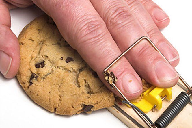Hand in a mousetrap with a cookie, illustrating a food-baited trap.