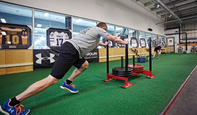 Athlete pushing a weighted sled on indoor turf in a training facility