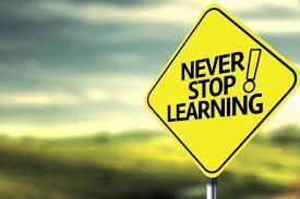 Yellow road sign reading “Never Stop Learning” against a blurred green landscape.