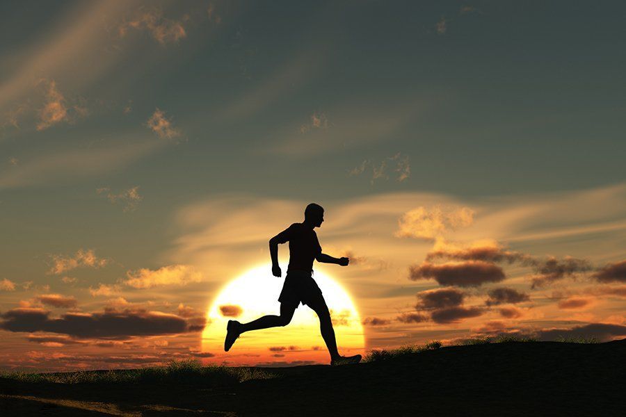 Silhouette of a runner at sunset against an orange sky and dark horizon