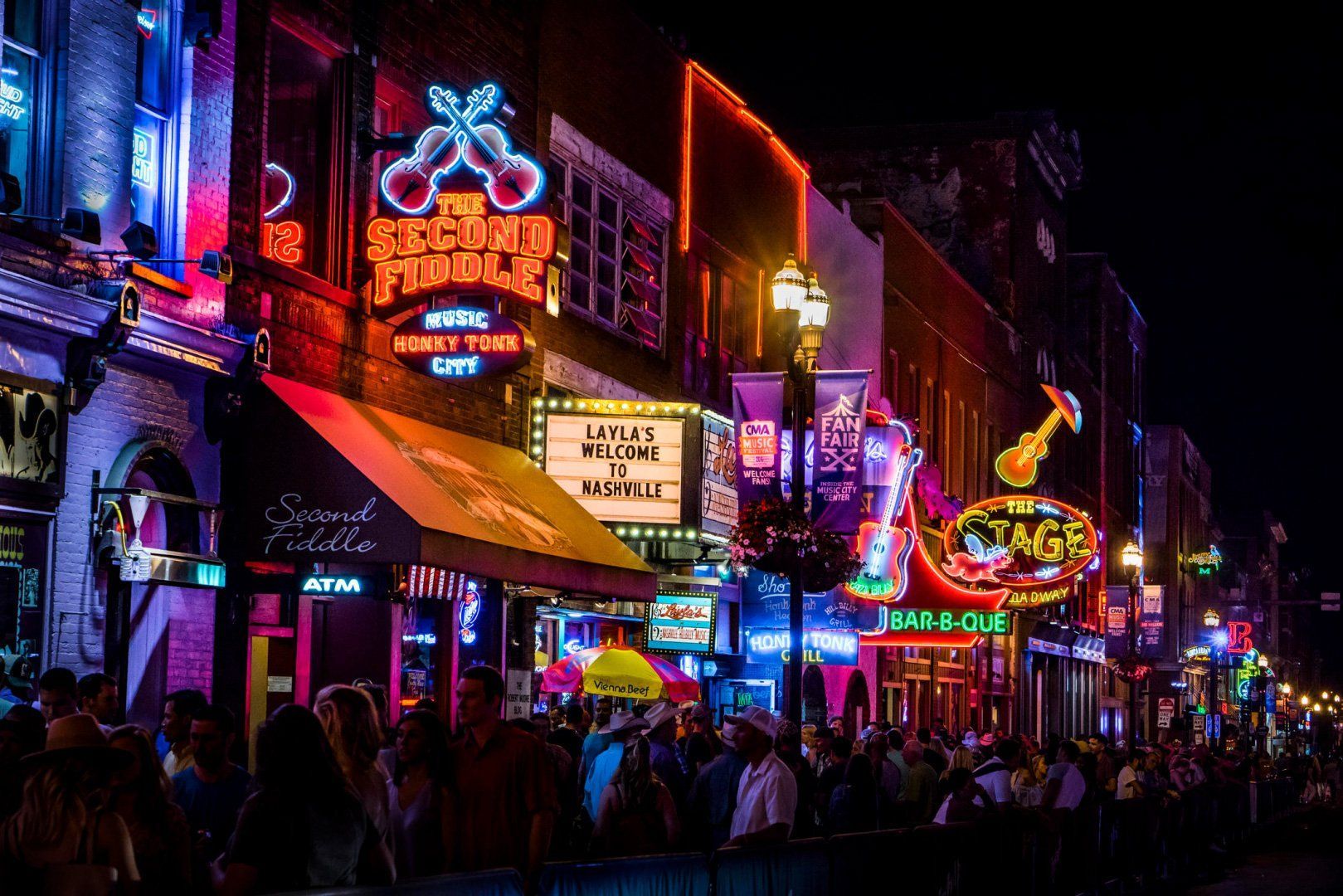 Neon-lit Bourbon Street at night with crowds, colorful bar signs, and festive lights