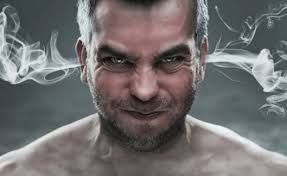 A man with a fierce expression exhales smoke against a gray background.