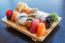 Assorted sushi rolls and nigiri on a wooden tray, arranged neatly on a dark table.